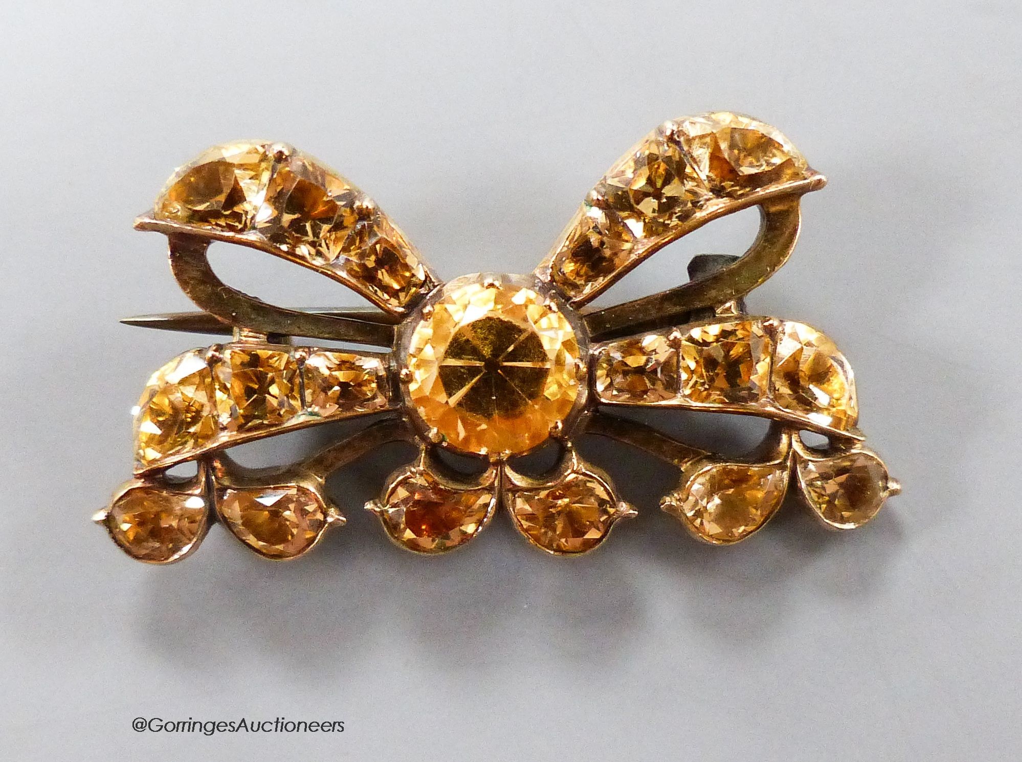 An early 20th century yellow metal and citrine cluster set ribbon bow brooch, with closed back setting, 30mm, gross 6.2 grams.